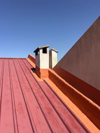 Cobertura em painel de chapa vermelha com a caleira e a base da chaminé impermeabilizadas