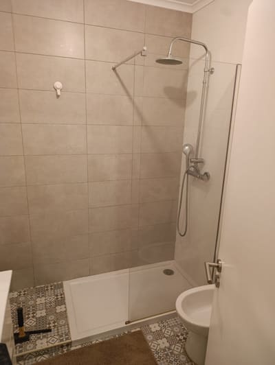 Casa de banho remodelada com base de duche, resguardo em vidro e pavimento em mosaico hidráulico